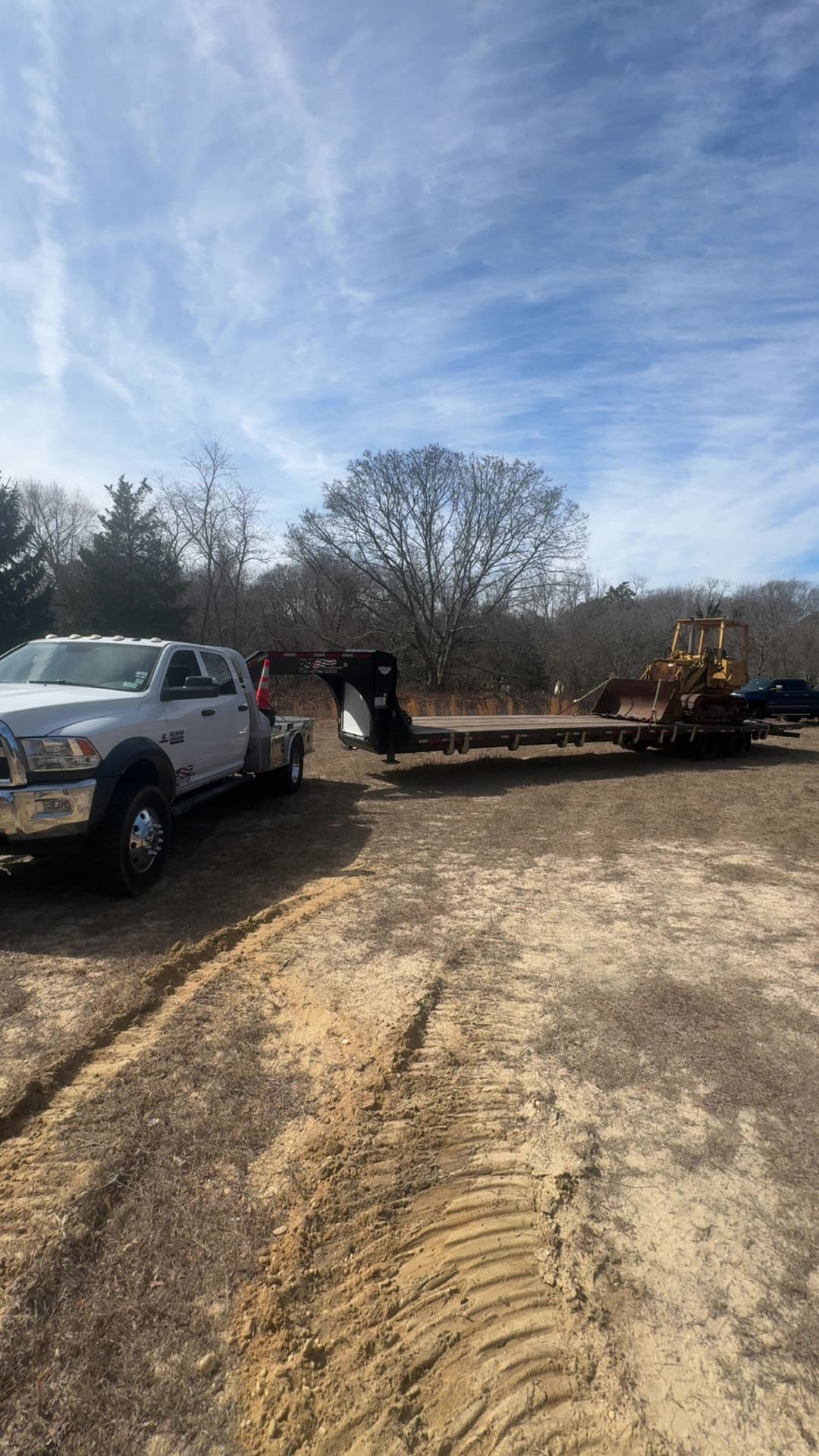 Truck towing heavy construction equipment on a flatbed in an open field.