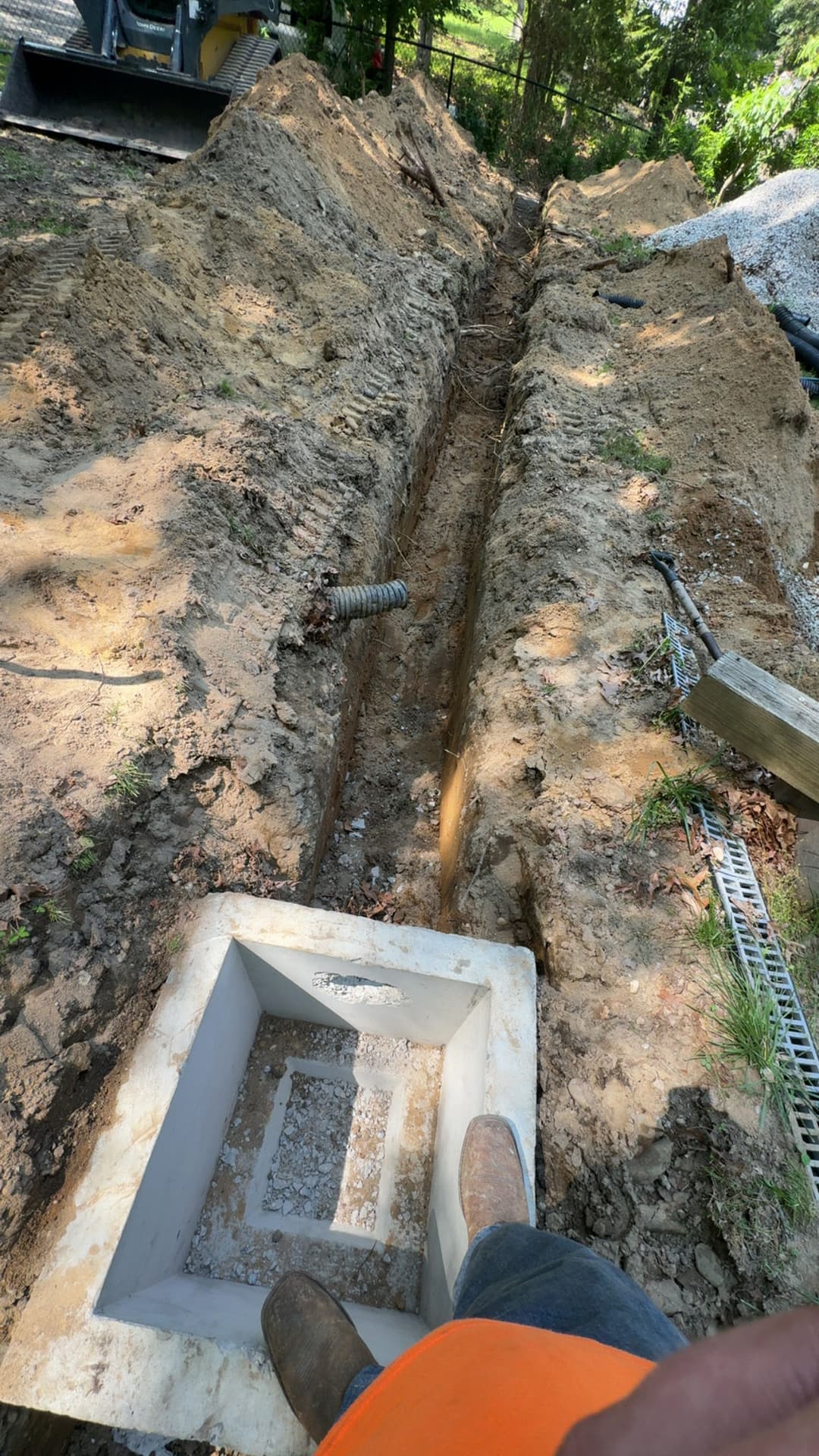 Excavated trench with concrete footer for construction project, surrounded by soil and machinery.