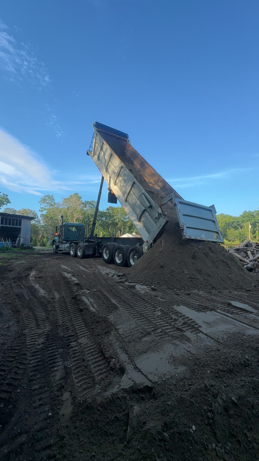 Dump truck unloading soil on construction site under clear blue sky.