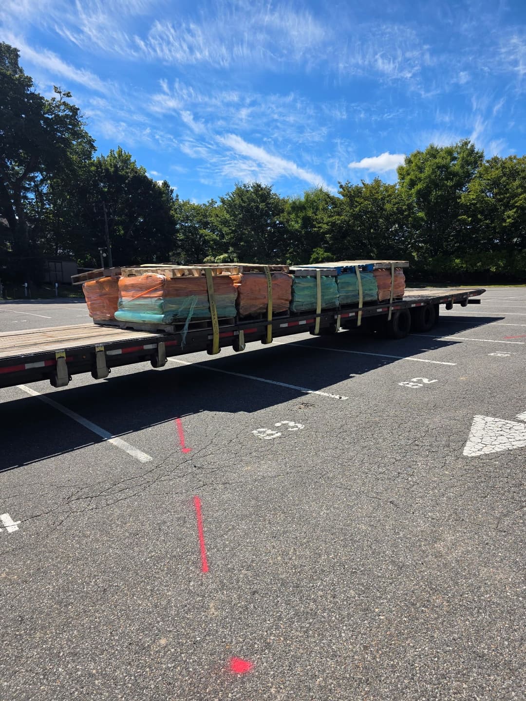 Flatbed truck carrying stacked construction materials in a parking lot.