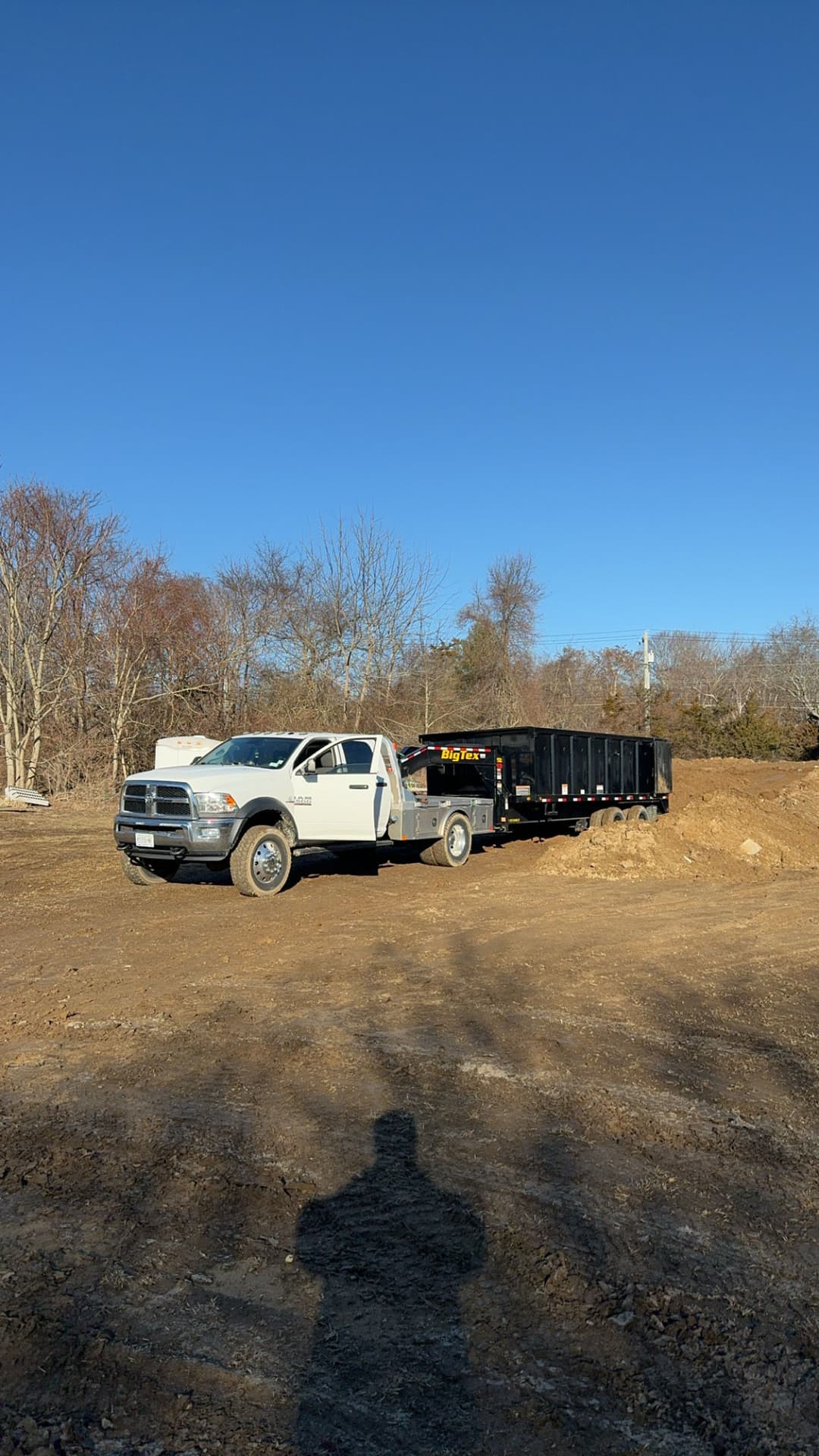 Dodge truck with a black dumpster on a construction site under a clear blue sky.