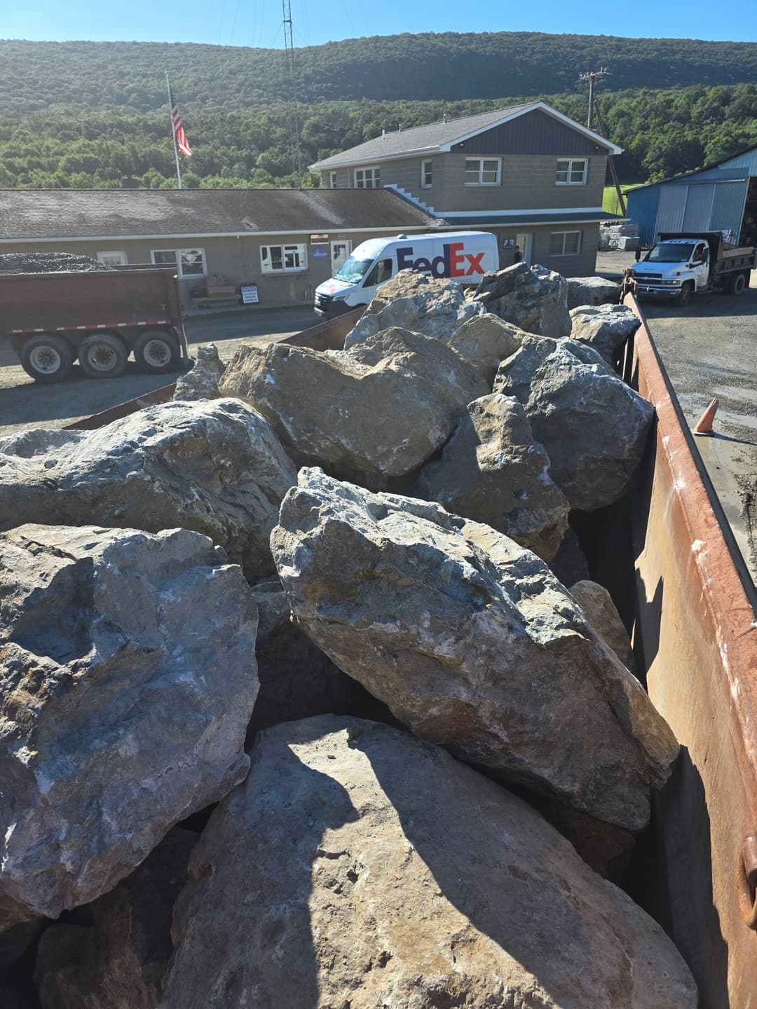 Large rocks in a truck bed with a FedEx van and a building in the background.