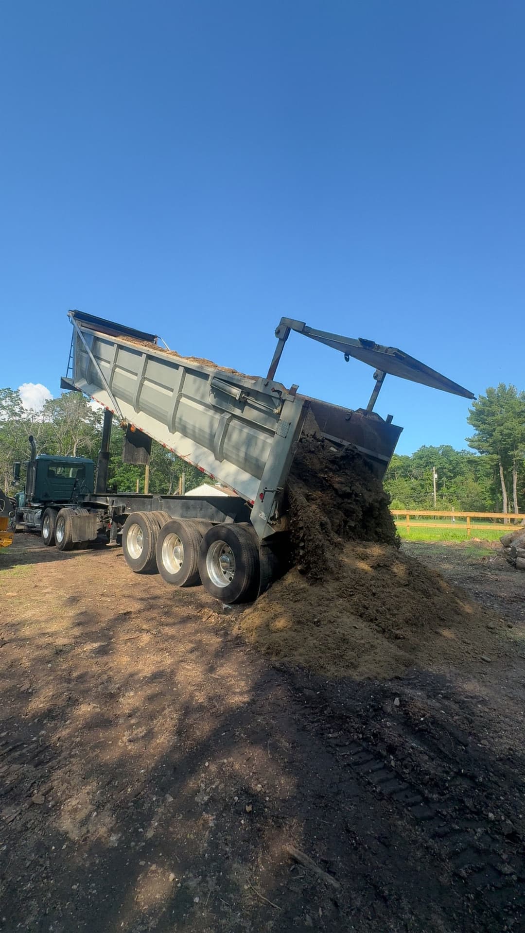 Dump truck unloading soil at a construction site under a clear blue sky.