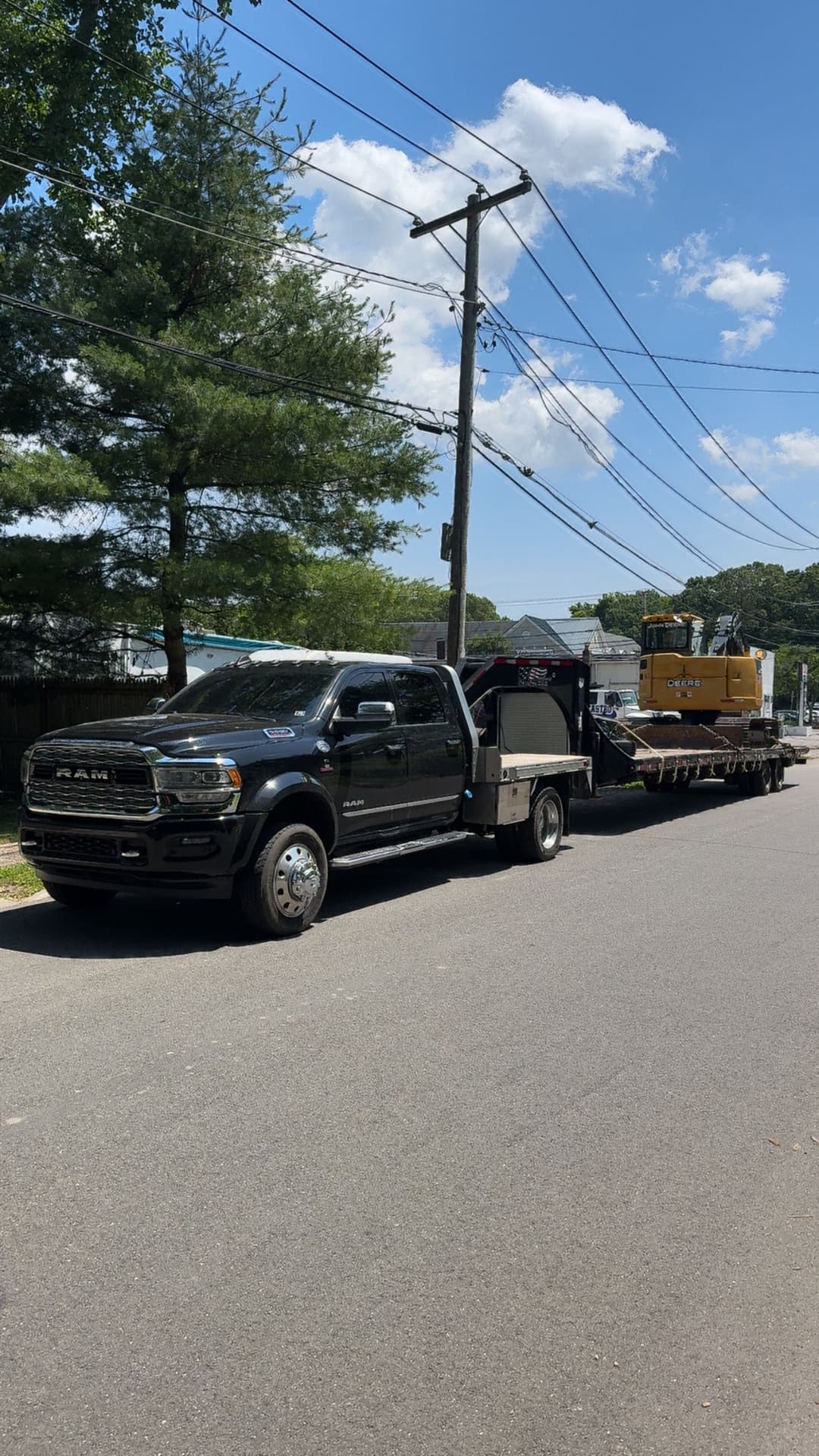 Black RAM truck towing a flatbed trailer with heavy construction equipment on a sunny day.