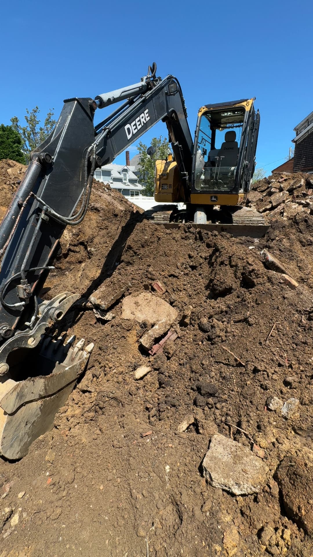 Excavator digging in a construction site with piles of dirt and debris under a clear blue sky.