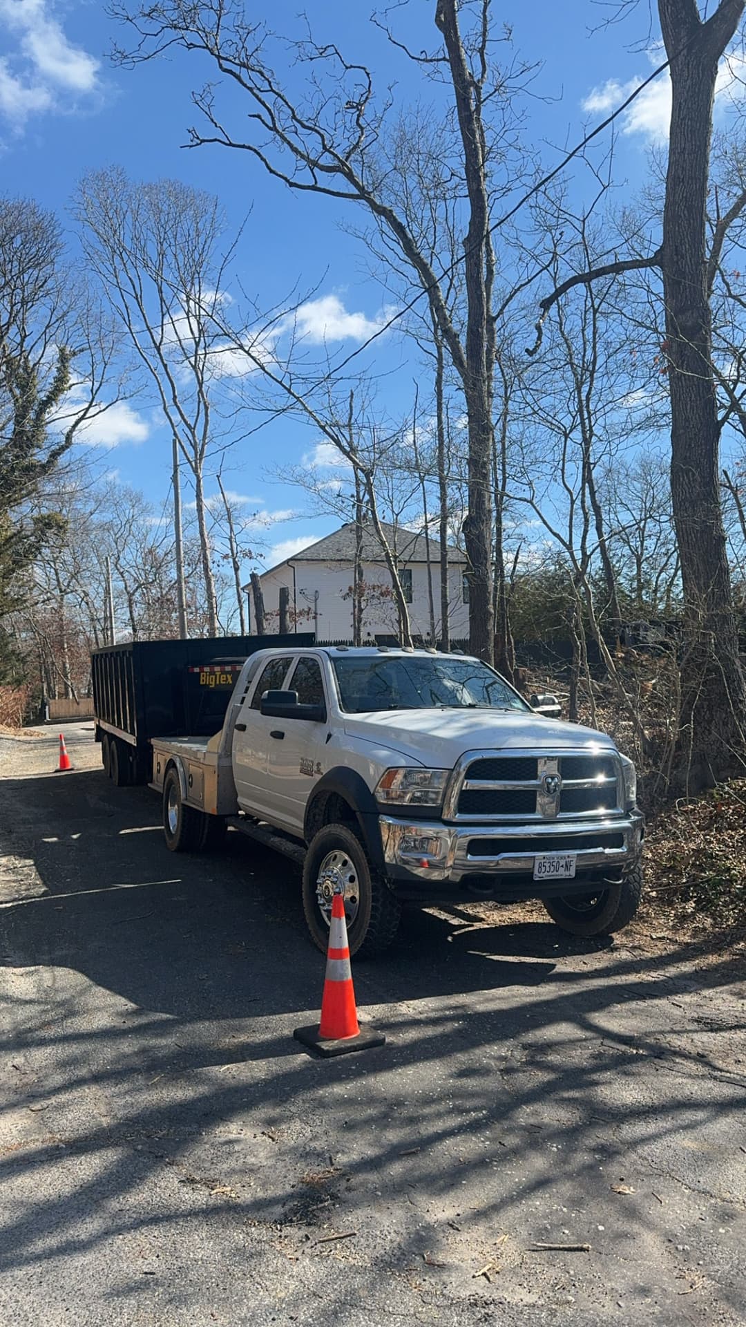 White pickup truck parked near a dumpster on a gravel road with orange cones and trees.