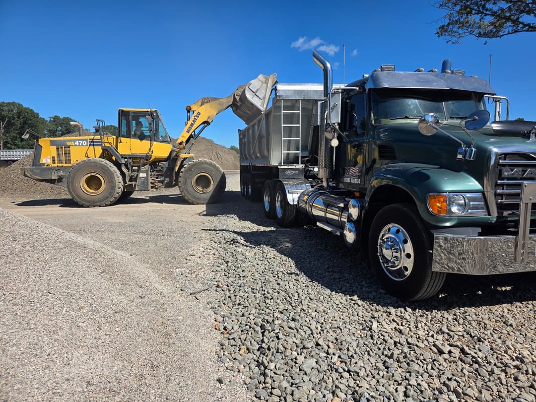 Heavy machinery loading gravel into a green dump truck on a construction site.