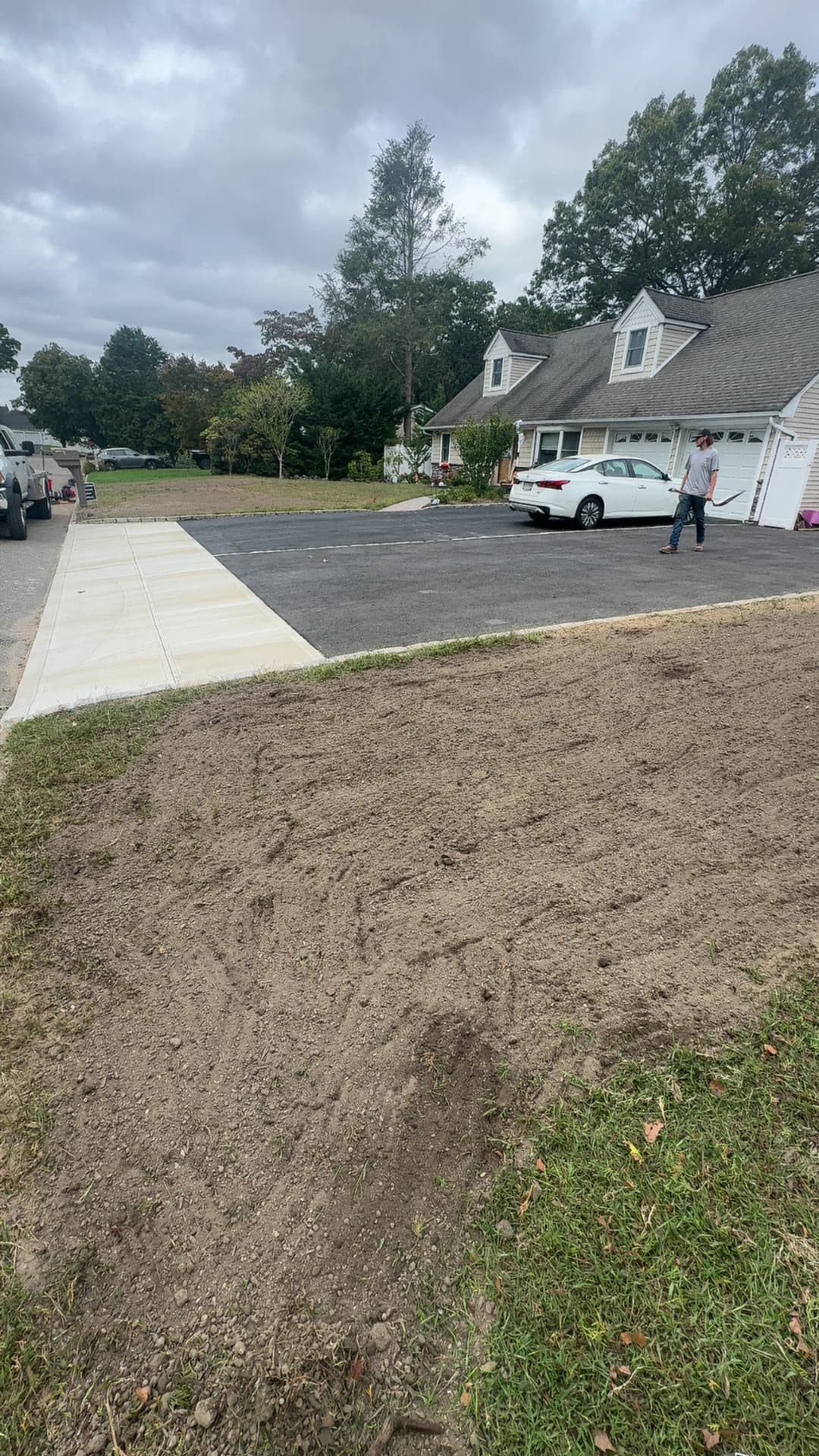 Residential construction site with freshly graded soil and parked cars in a suburban neighborhood.