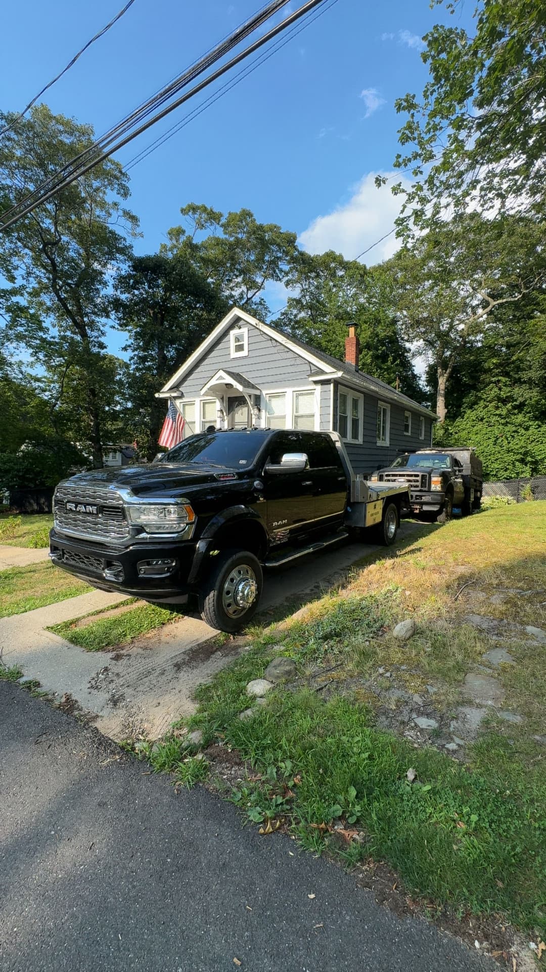 Black RAM pickup truck parked in front of a gray house with an American flag and trees.