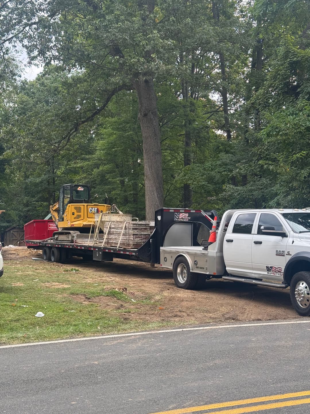 Construction truck and equipment on a trailer in a wooded area, ready for excavation work.