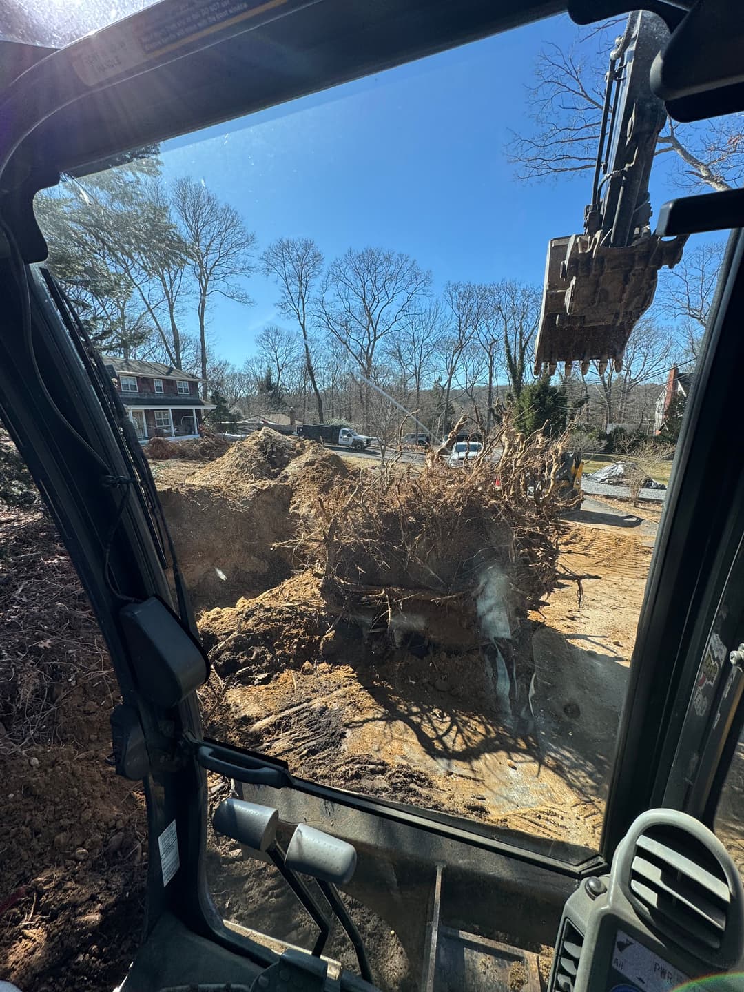 Excavator view of uprooted tree stump at a construction site under clear blue sky.
