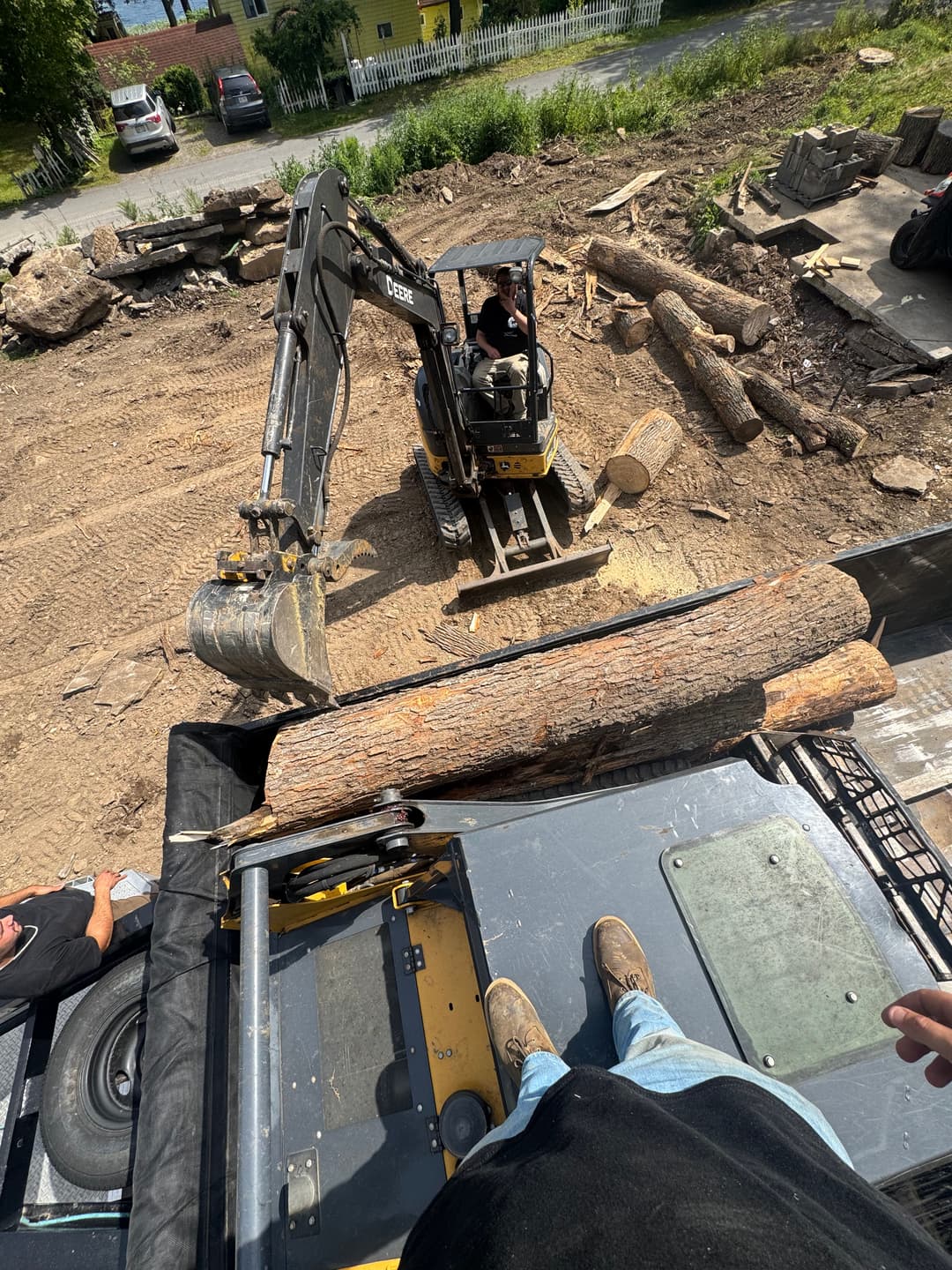 Construction worker using a mini-excavator to lift logs on a jobsite.
