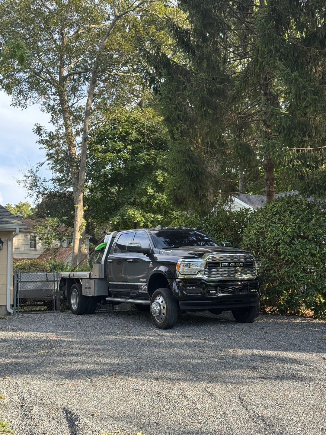 Black truck parked in a gravel driveway surrounded by trees and greenery.