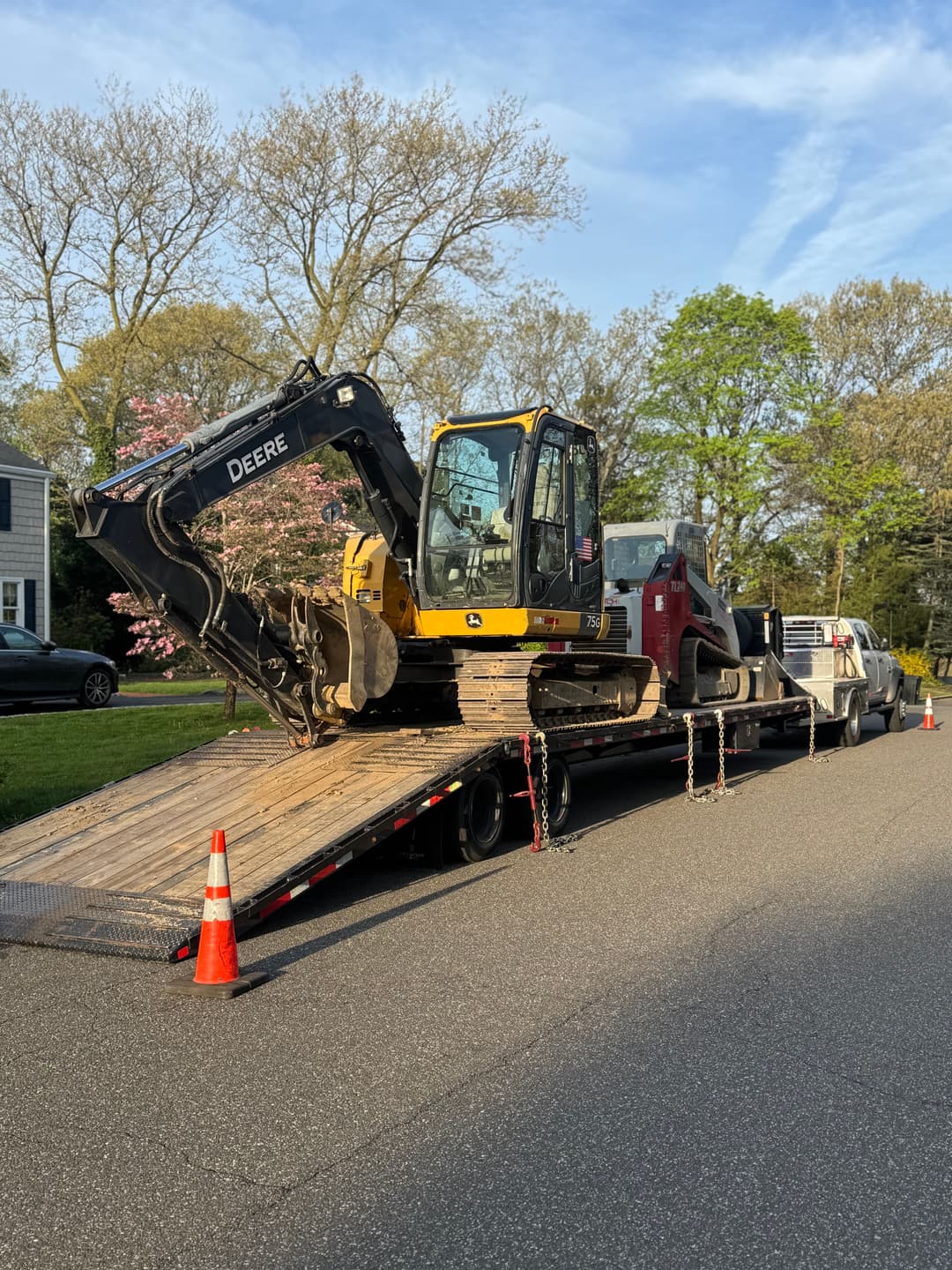 Excavator and construction equipment on a flatbed truck parked on a residential street.