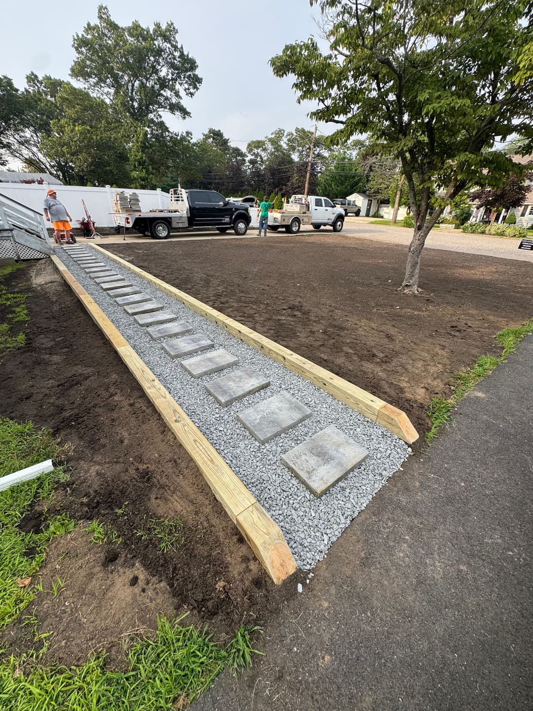 Gravel walkway with stone pavers leading to a driveway and parked trucks in a residential area.