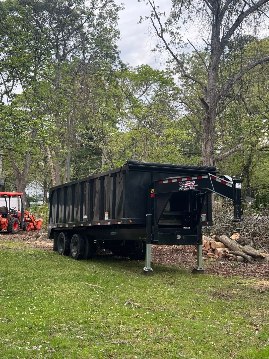 Black dump truck parked in a wooded area, ready for debris removal and landscaping projects.
