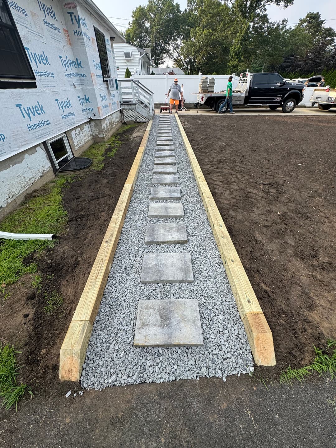 Stone pathway installation lined with wooden framing and gravel, enhancing outdoor landscaping.