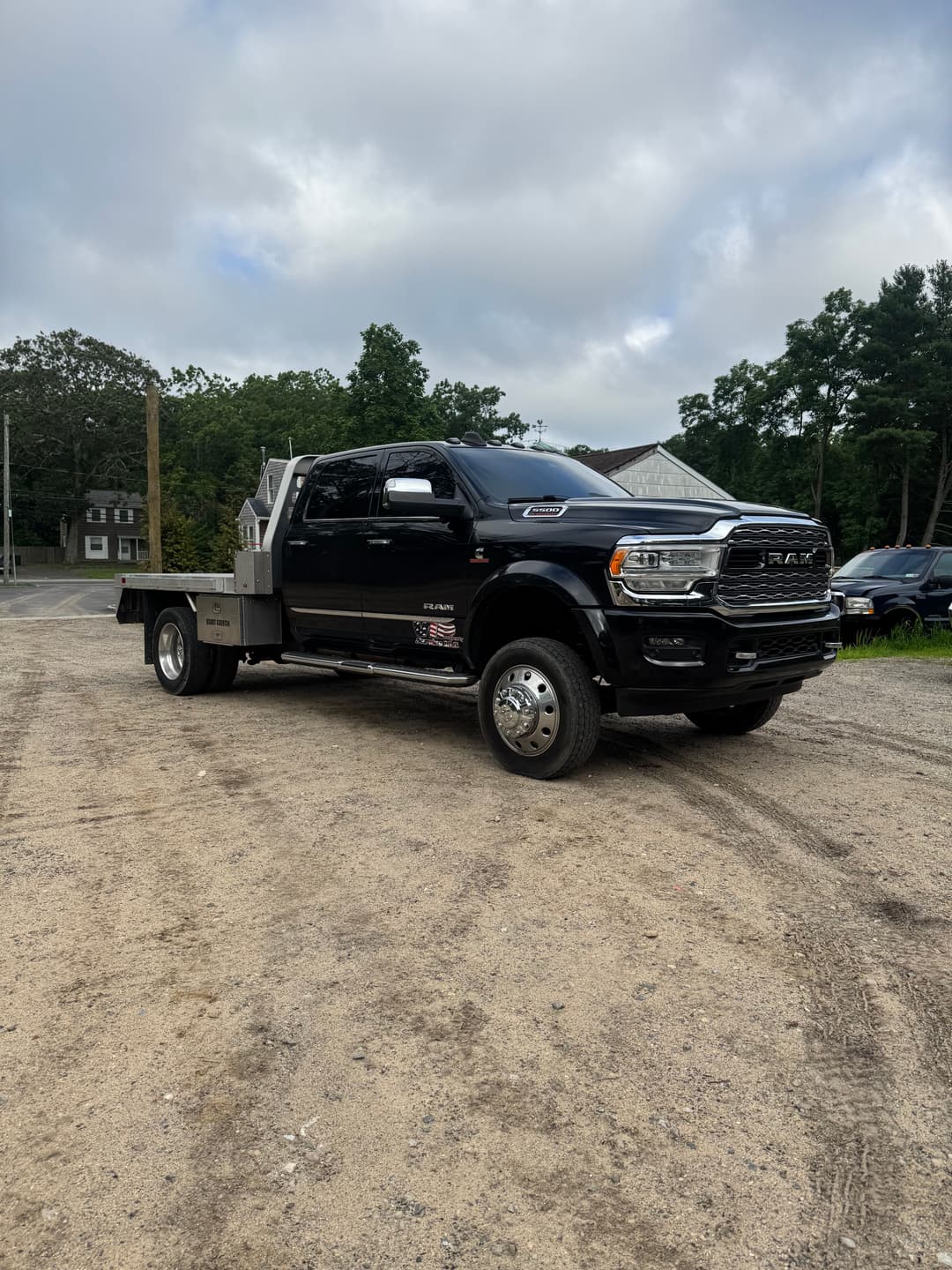 Black Ram truck with a flatbed, parked on gravel with trees in the background.