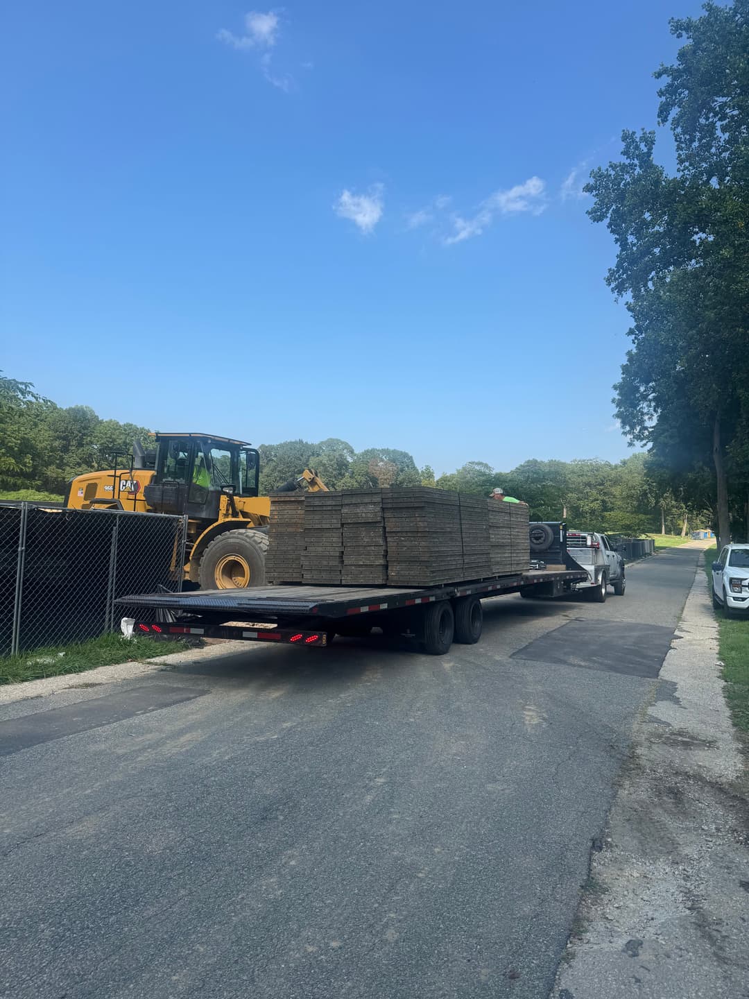 Flatbed truck delivering construction materials on a residential road with machinery in background.