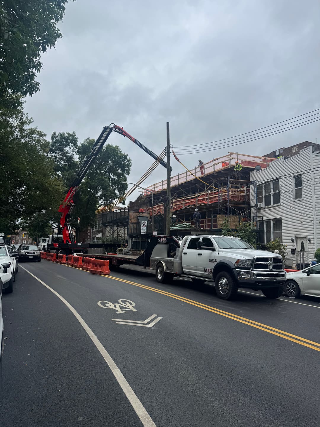 Construction site with crane lifting materials beside a busy street. Workers on scaffolding.