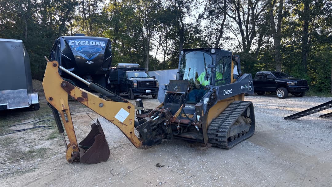 John Deere 35D excavator on gravel lot with trucks and trailers in background.