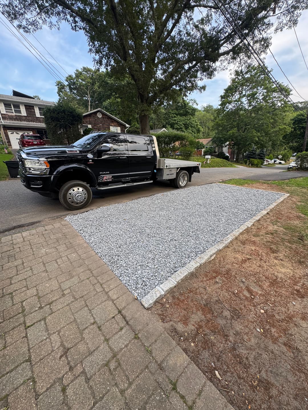 Black pickup truck parked on gravel driveway with stone edging in a suburban setting.