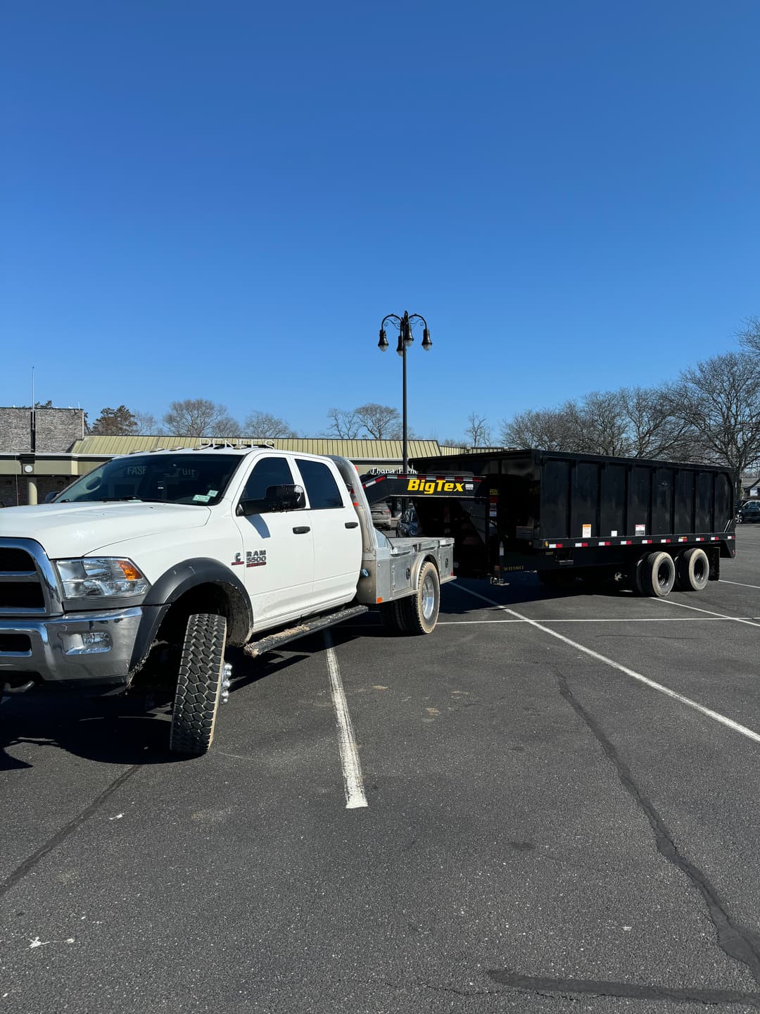 White truck towing a Big Tex trailer in a parking lot under clear blue sky.