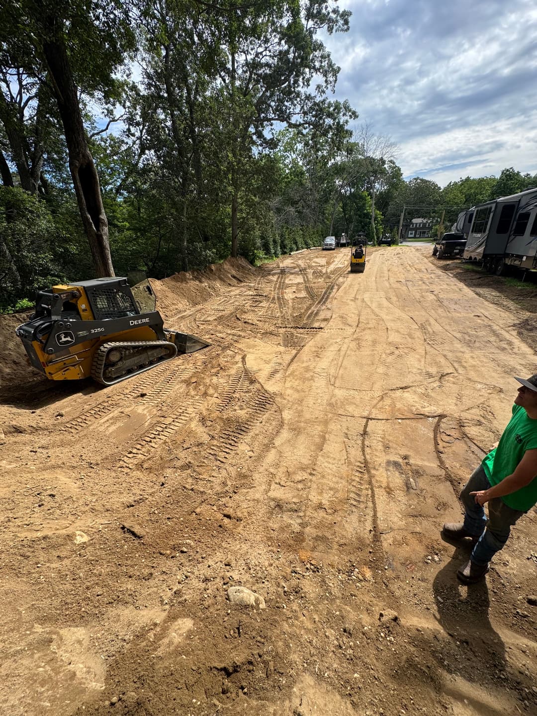 Construction site with machinery on dirt road, trees in background, and worker observing.