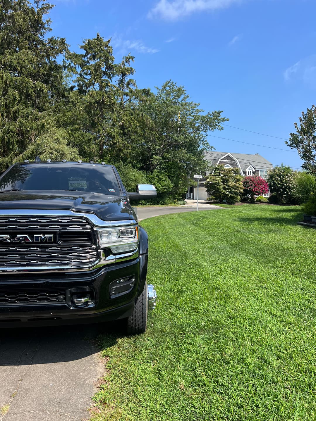 Black RAM truck parked on a green lawn near a house with trees and blue sky.