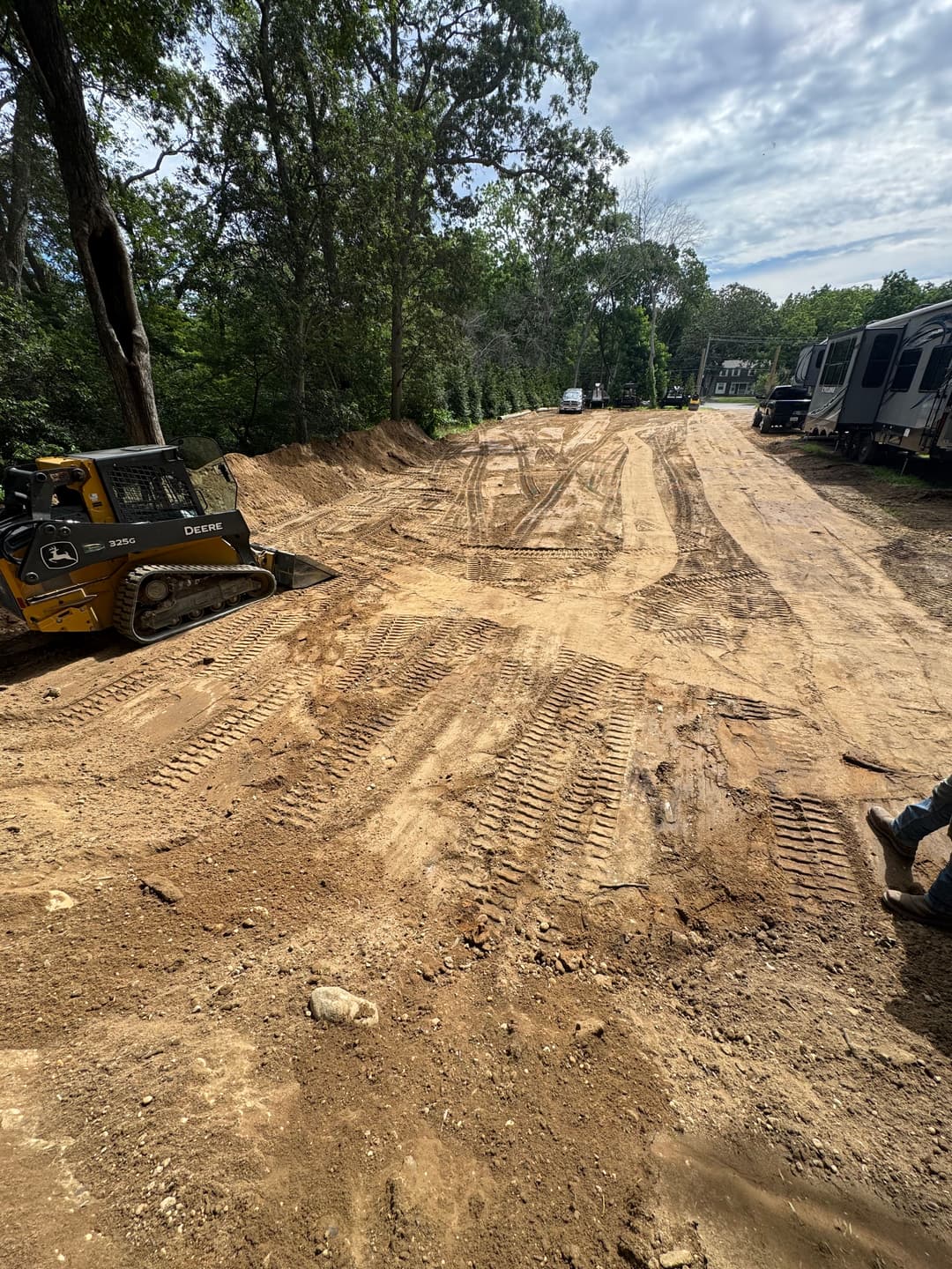 Construction site with a bulldozer on a dirt road surrounded by trees and RVs.