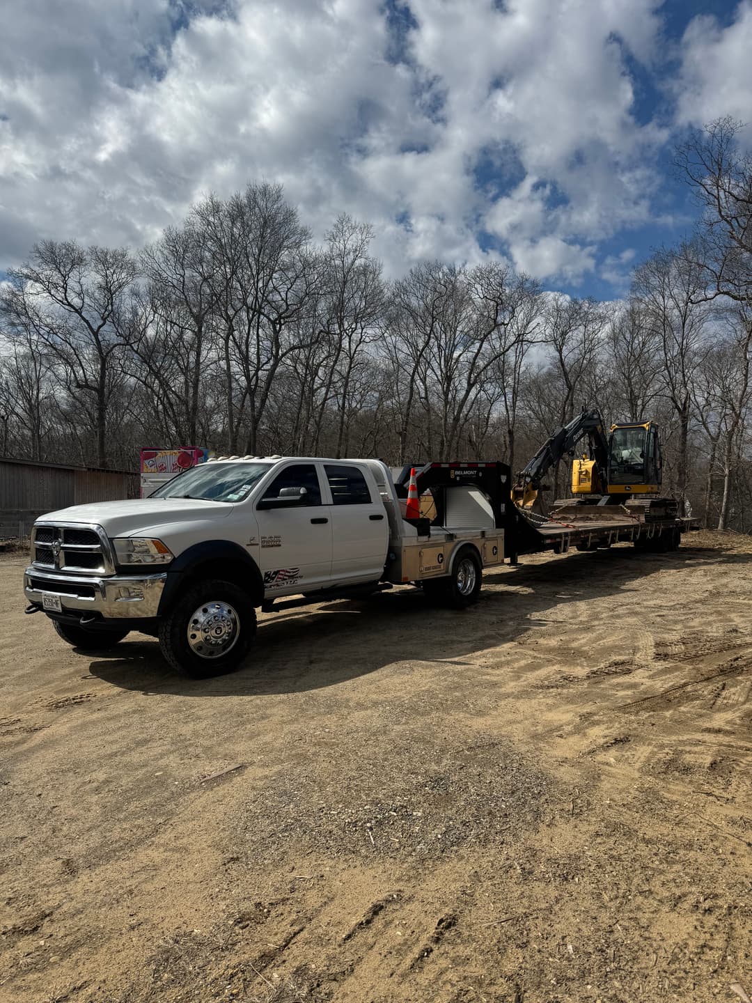 Truck with trailer carrying an excavator on a construction site under a cloudy sky.