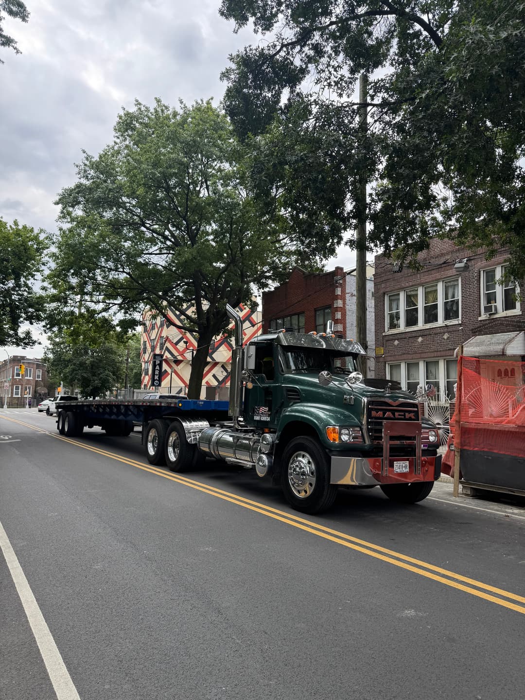 Mack truck parked on a city street beside a mural and construction site.