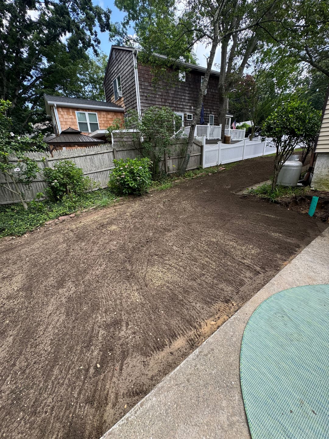 Freshly prepared backyard soil ready for landscaping, bordered by trees and residential houses.