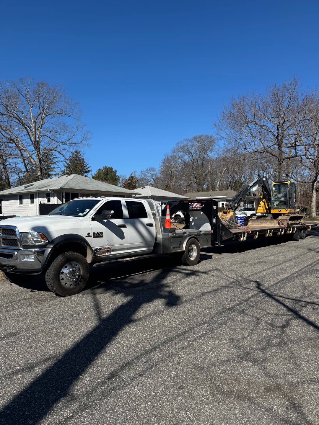 White pickup truck with equipment trailer, parked on a residential road under clear blue sky.