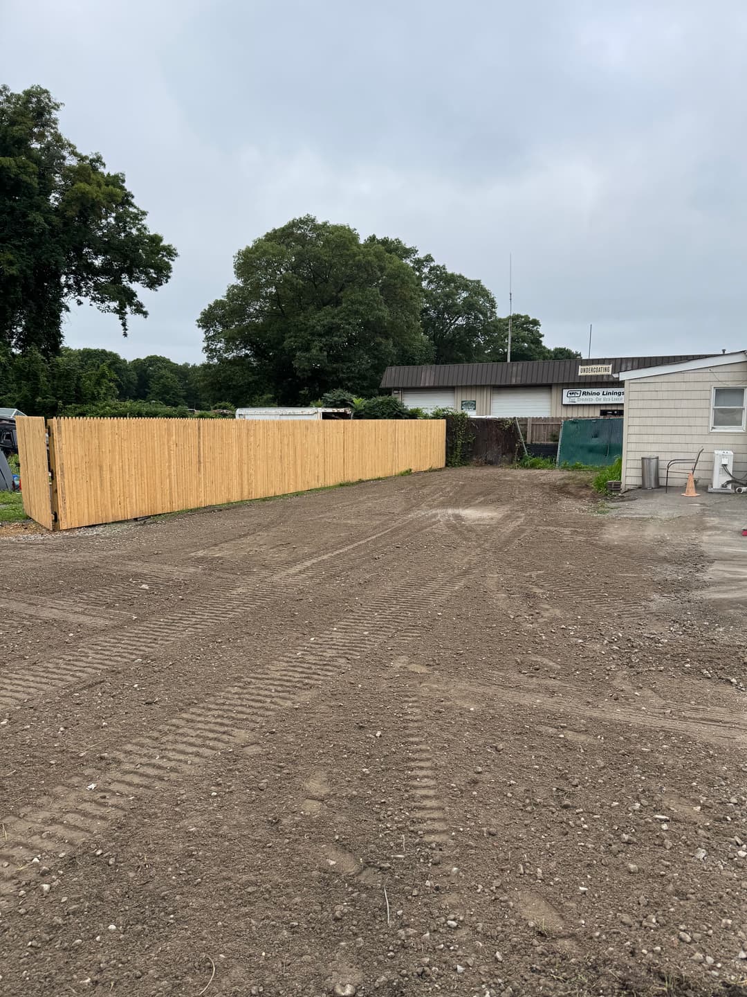 Newly constructed wooden fence along a gravel driveway near a commercial building.