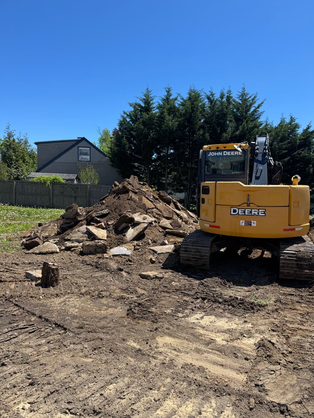 Excavator near a pile of rocks and dirt on a construction site under a clear blue sky.