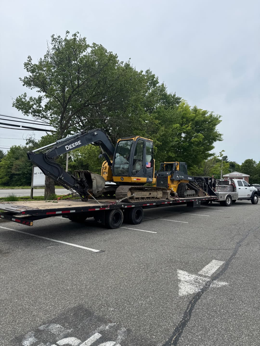 Yellow John Deere excavators loaded on a flatbed truck in a parking lot.