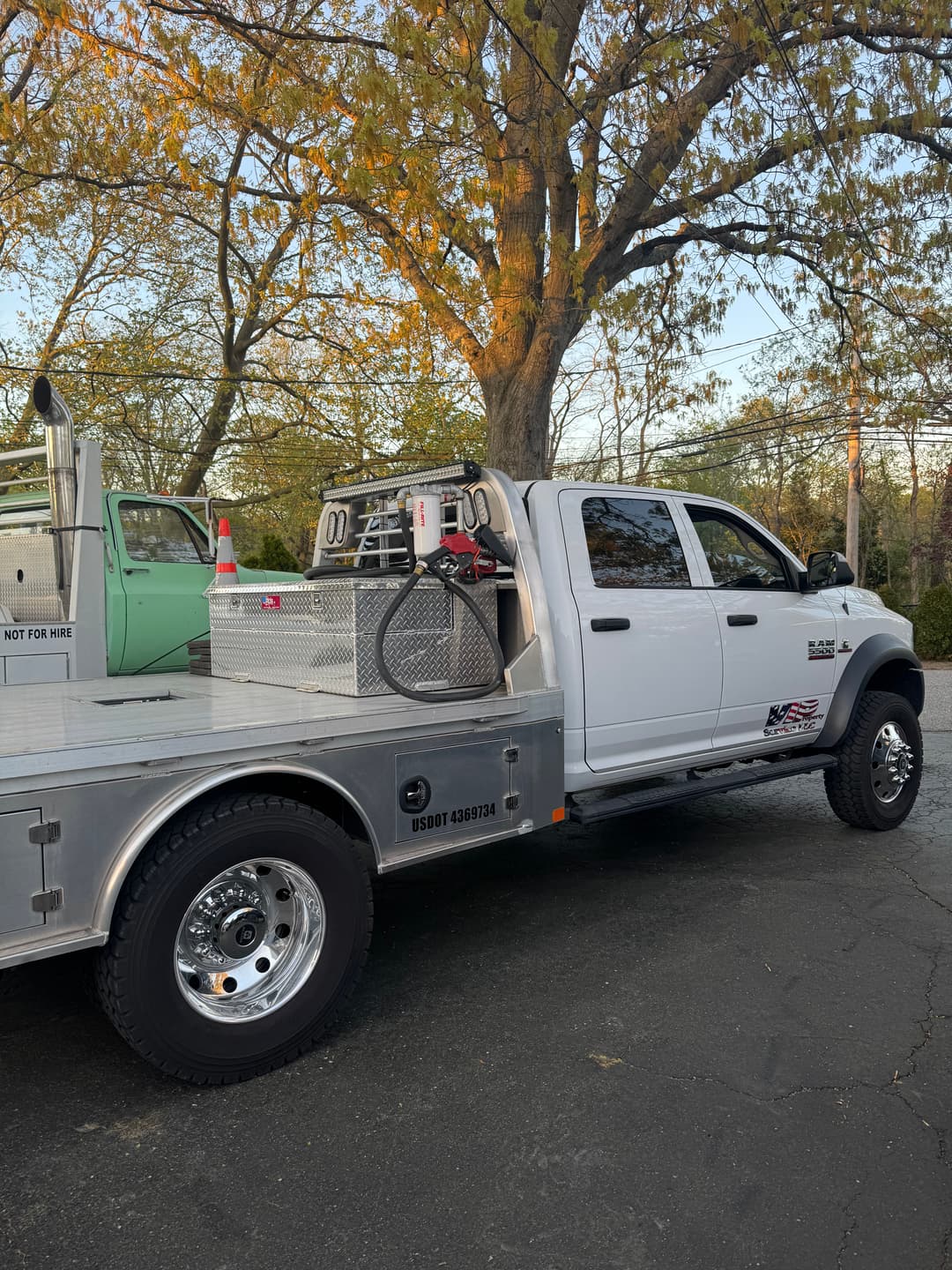 White utility truck with aluminum bed and equipment storage near trees in a parking lot.