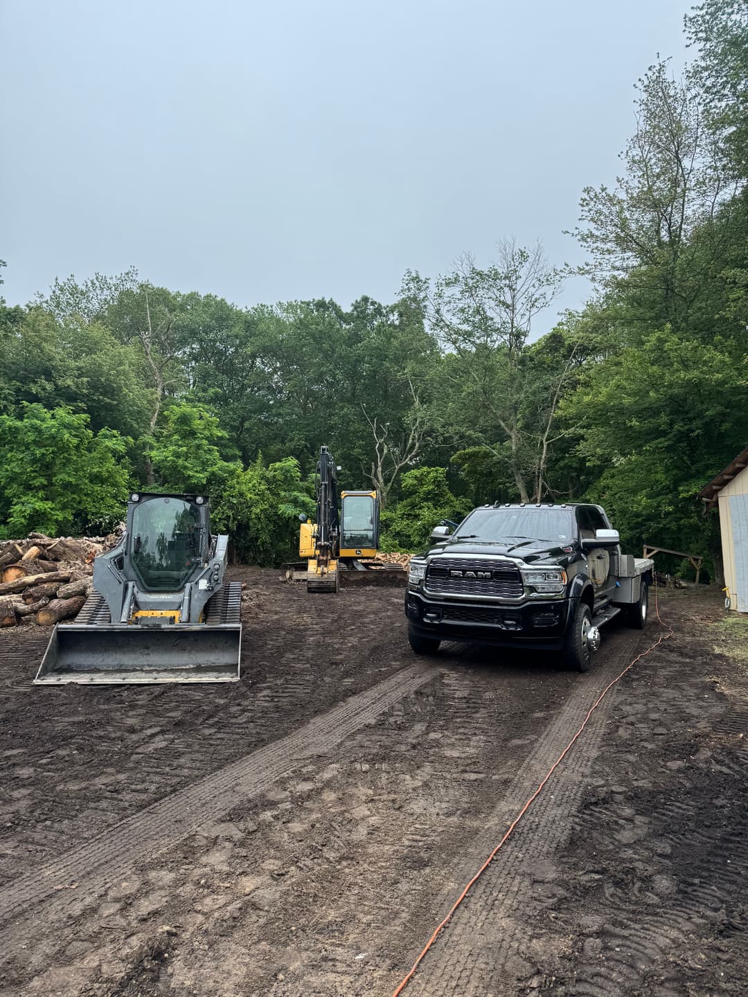 Black pickup truck and construction equipment on a dirt lot surrounded by trees.