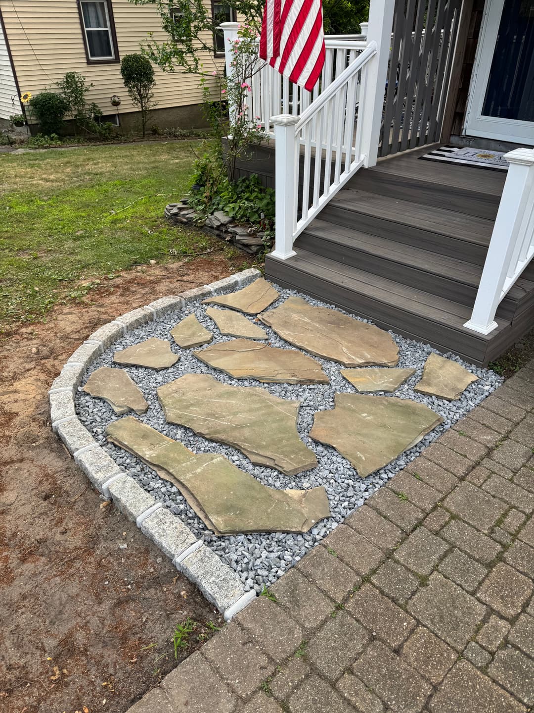 Flagstone path with gravel and border stones leading to a house entrance with a porch.