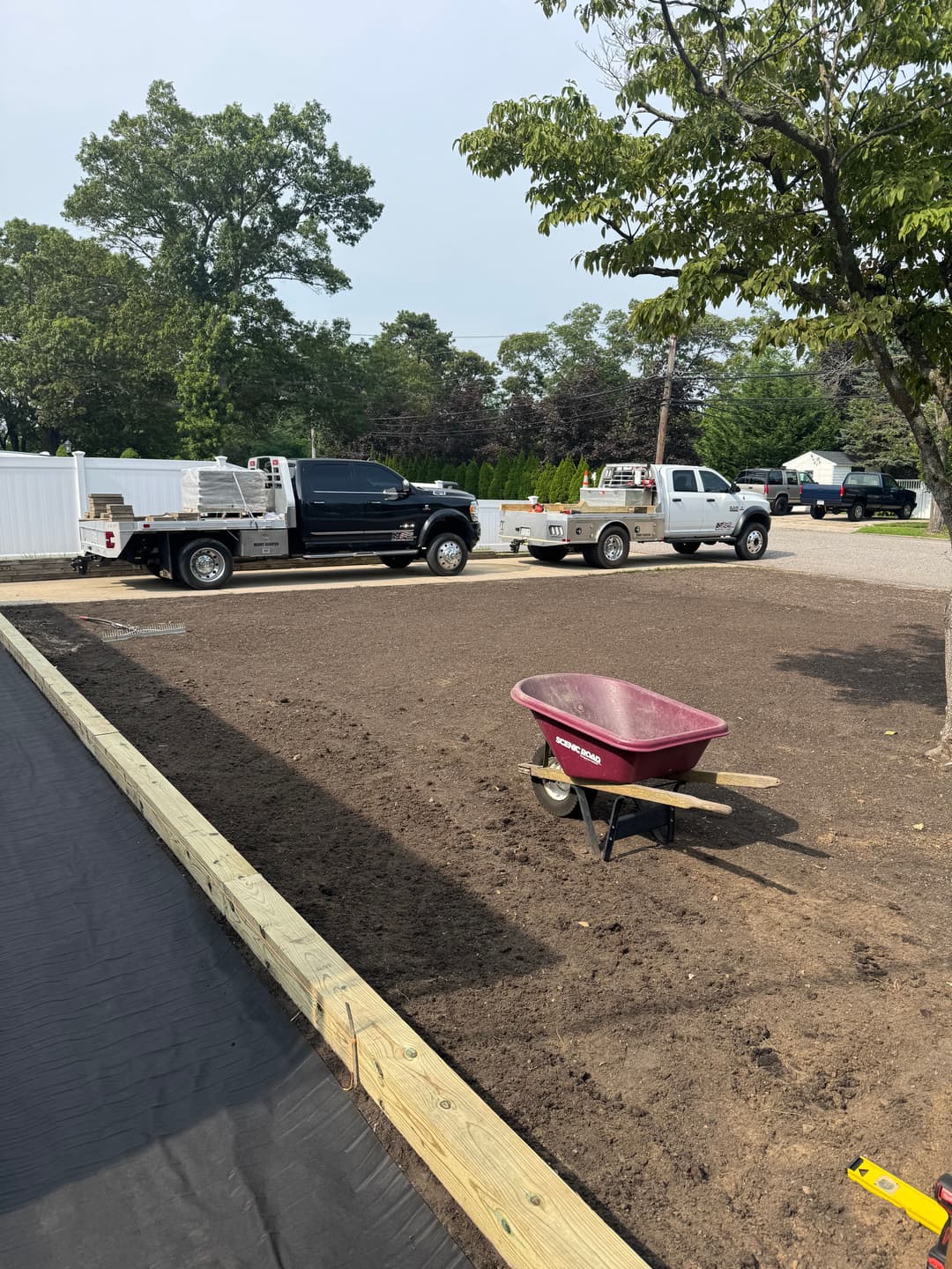 Construction site with wheelbarrow, trucks, and prepared soil for landscaping project.