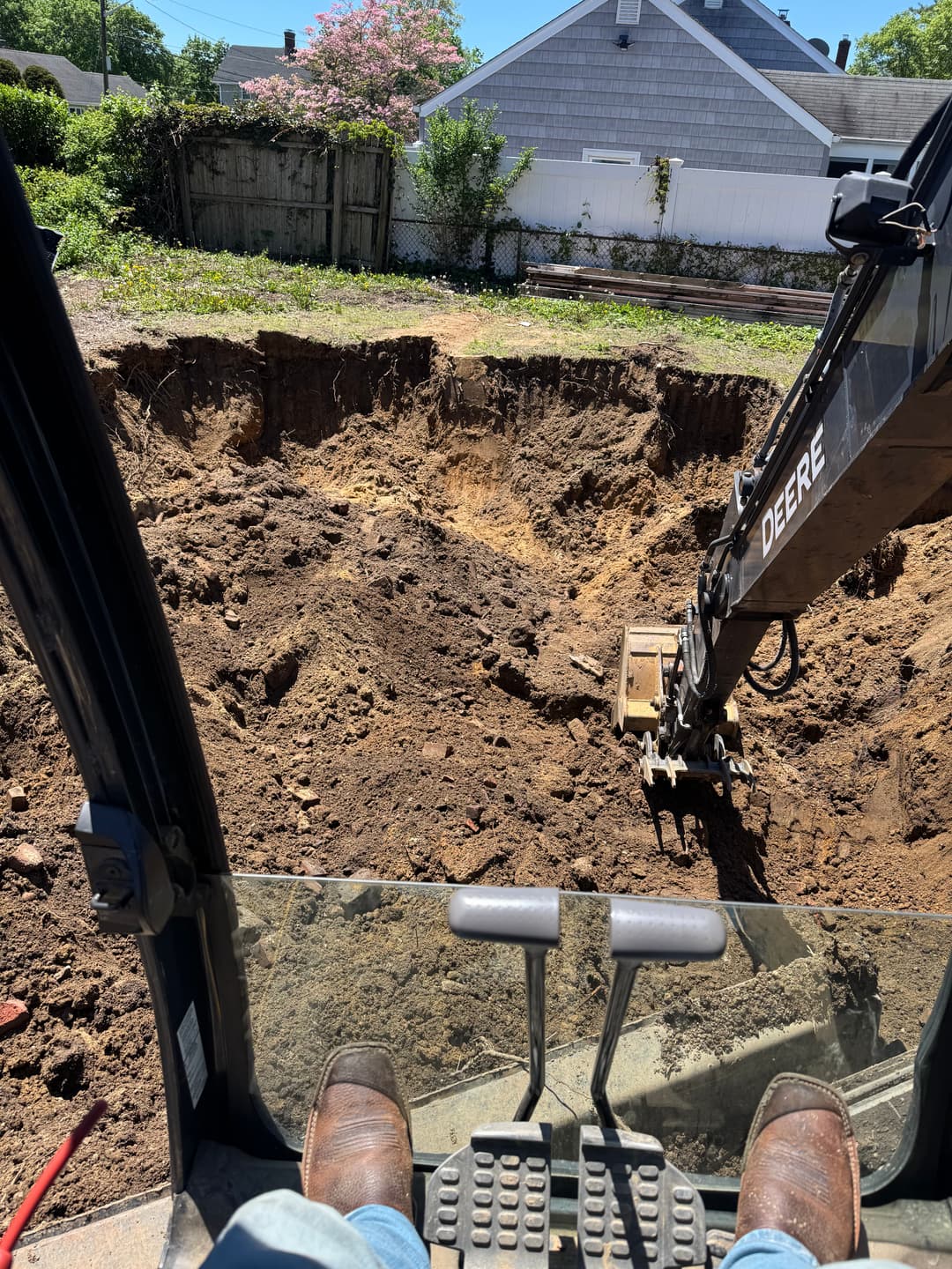 Excavator operator's view of a large dug hole in a residential yard with construction site details.
