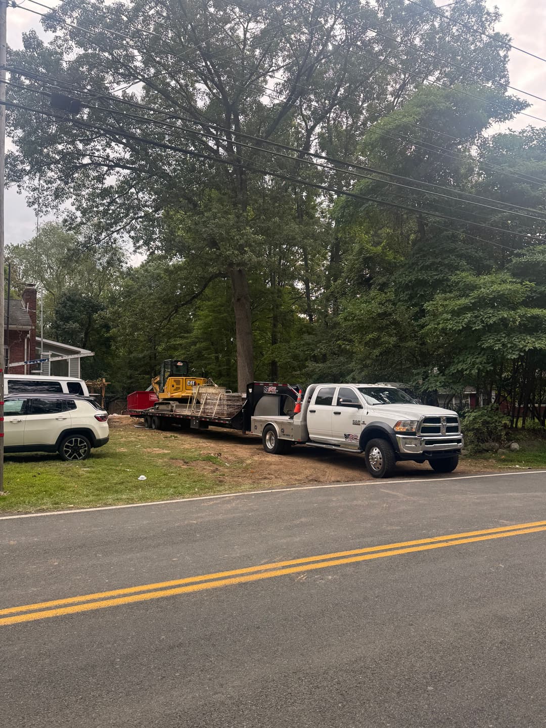 Pickup truck with trailer transporting construction equipment in a residential area.