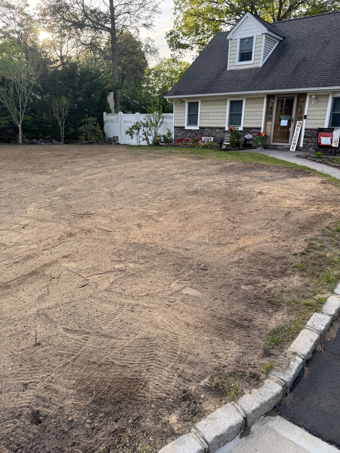 Cleared front yard with freshly turned soil and a house in the background, ready for landscaping.