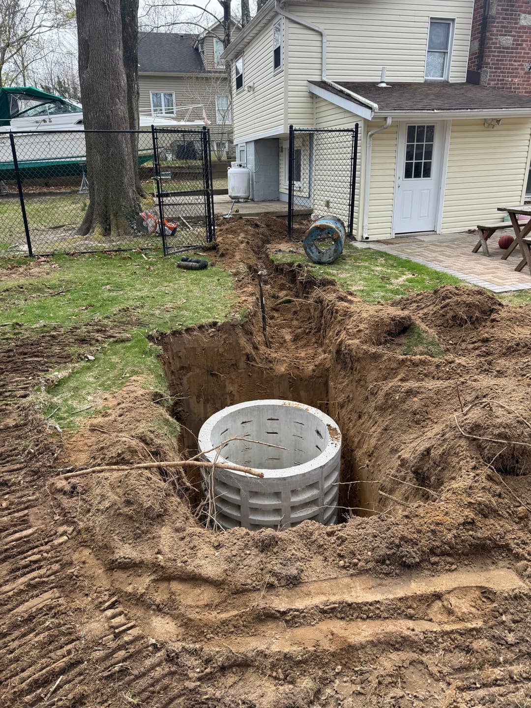 Excavation in backyard showing a buried concrete structure, fence, and house exterior.