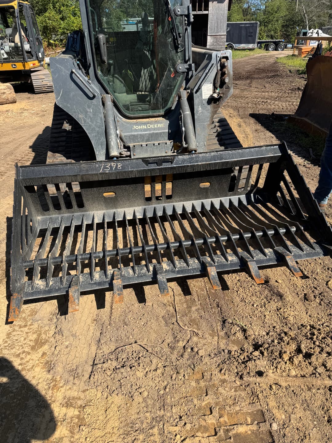 John Deere skid steer with a heavy-duty grapple attachment on a construction site.