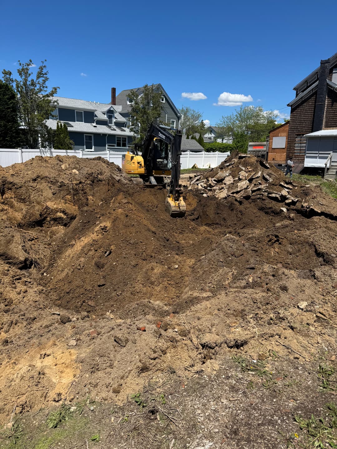 Excavator digging in construction site with mound of dirt and debris on a sunny day.