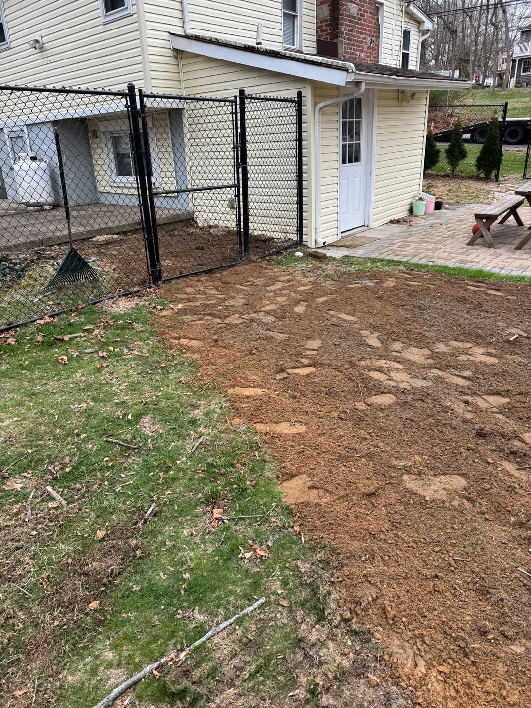 Yard renovation with freshly tilled soil and fence beside a house and patio area.