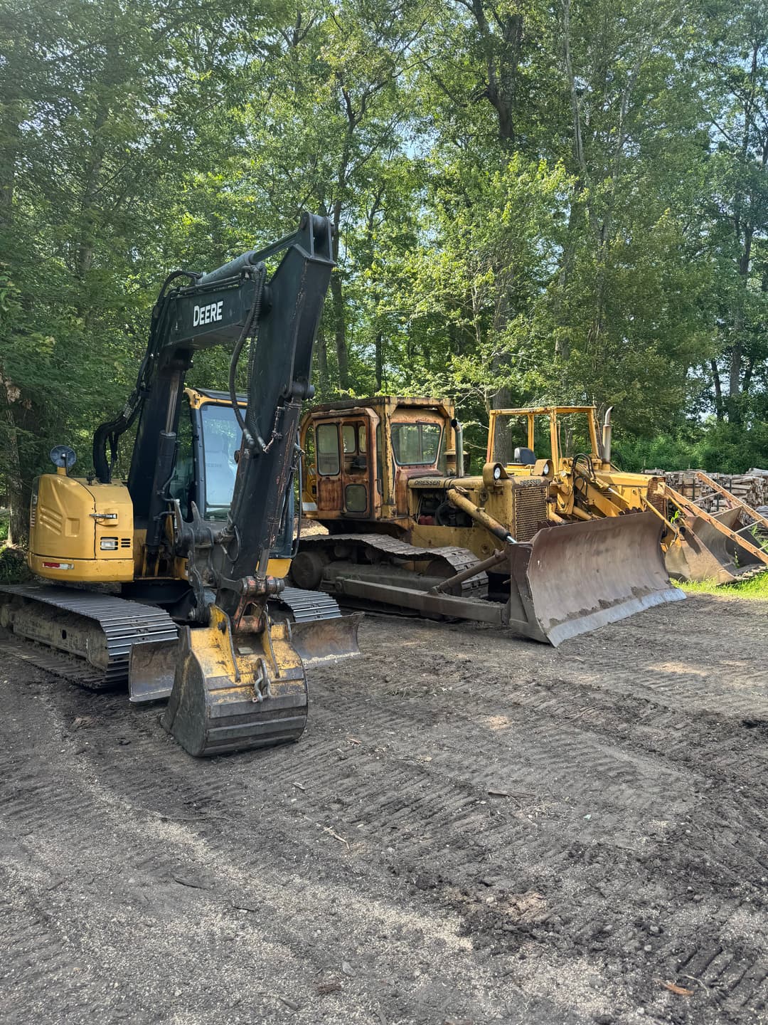 Excavators and bulldozers parked in a forest clearing, surrounded by trees and dirt.