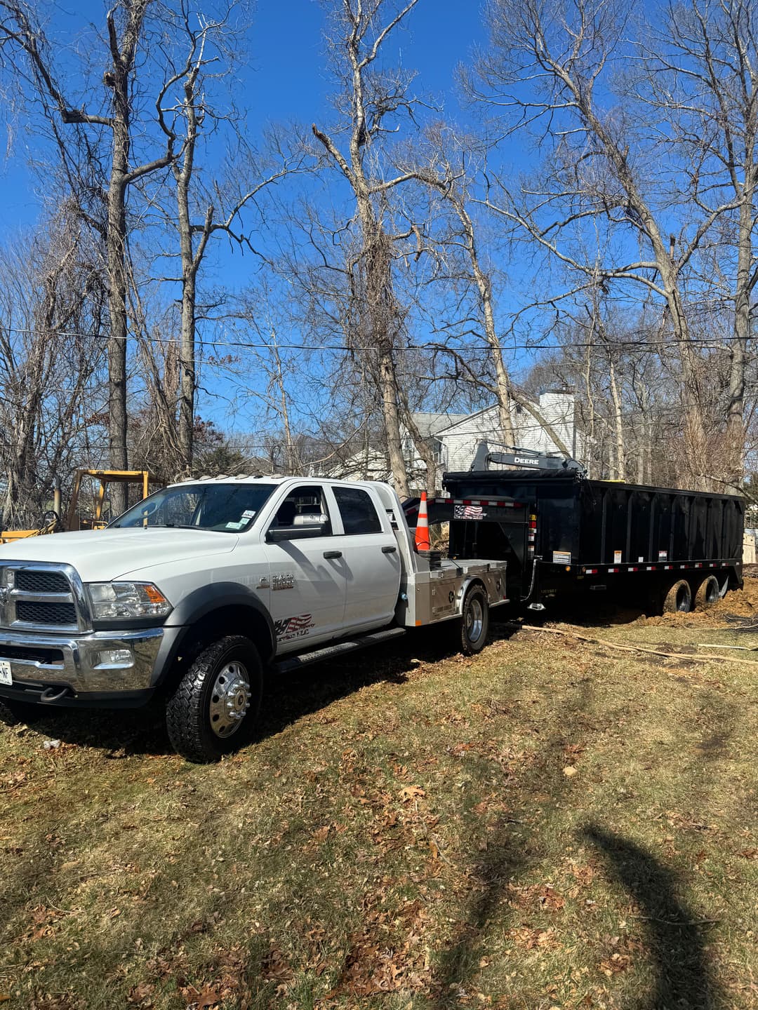 White pickup truck towing a black dump trailer on a sunny day in a wooded area.